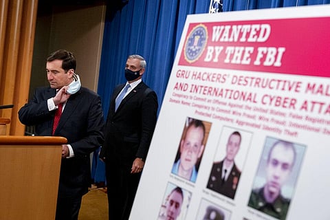 A poster showing 6 wanted Russian military intelligence officers is displayed as Assistant Attorney General for the National Security Division John Demers, left, takes the podium to speak. (Photo |AP)