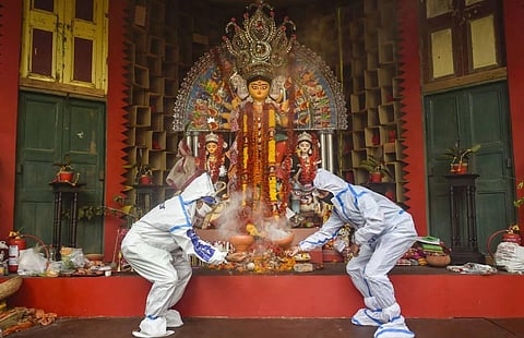 Devotees wearing PPE kits perform the traditional 'Dhunuchi dance' in front of an idol of Goddess Durga during Durga Puja festival in Kolkata. (Photo | PTI)