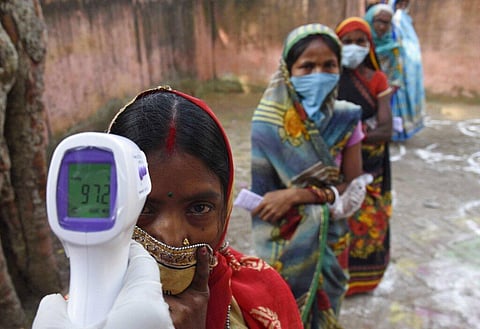 An election officer checks the temperature of a voter before allowing voters to pass at a polling station, during the first phase of state elections at Paliganj, Bihar. (Photo | AP)