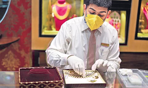 An attendant cleans a jewellery item before display at a Tanishq showroom .