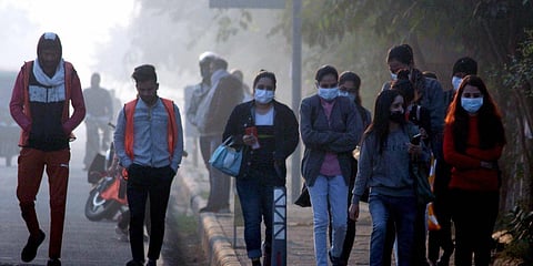 Commuters wearing warm clothes walk on a street on a cold winter morning in Gurugram. (photo| PTI)
