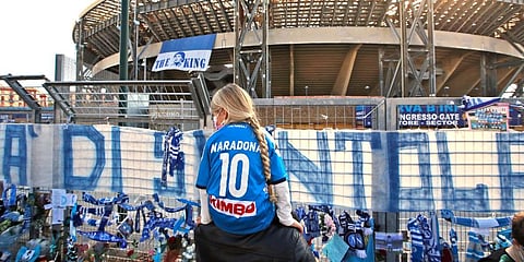A girl sits on a man's shoulders as she looks at gadgets and memorabilia commemorating soccer legend Diego Maradona outside the San Paolo stadium, in Naples, southern Italy. (Photo | AP)