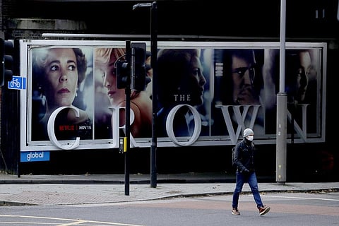 A man wearing a face mask walks past a billboard advertising 'The Crown' television series about Britain's Queen Elizabeth II and the royal family. (Photo | AP)