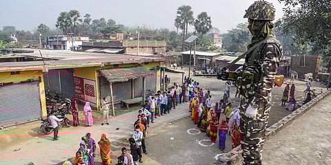 A security personnel stands guard as voters wait in a queue to cast their vote during the third phase of Bihar Assembly Elections, at a polling station in Vaishali, Saturday. (Photo | PTI)