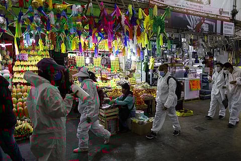 Workers wearing protective suits walk to take up positions to dispense antibacterial gel to passing shoppers and workers, inside the Central de Abastos. (Photo | AP)