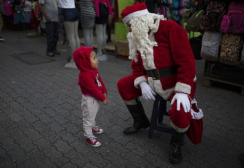 Fredy Parra, dressed as Santa Claus, speaks to a girl at a Christmas fair in Venezuela. For over 10 years, children have had their picture taken with Parra at the fair for a small fee. (Photo | AP)