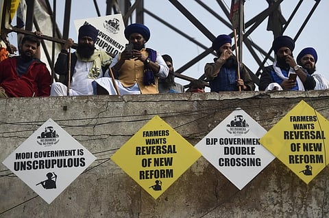 Farmer stand on top of a building as placards are seen hanging during a protest against the central government’s recent agricultural reforms at the Delhi-Haryana state border in Singhu. (Photo | AFP)