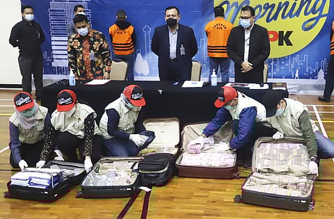 Officers arrange suitcases full of rupiah and U.S. dollar bills confiscated from suspects as Chairman of Indonesia's Corruption Eradication Commission Firli Bahuri, top center, looks on. (Photo | AP)