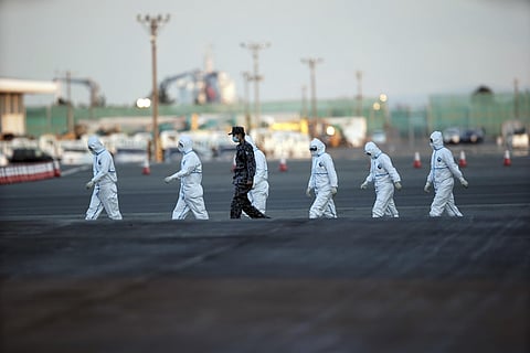 Officials with protective suites walk from the quarantined cruise ship Diamond Princess in Japan's Yokohama Port. (Photo | AP)