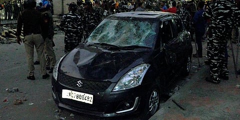 Paramilitary personnel stand guard near a damaged car after demonstrators of the two groups started pelting stones at each other, at Maujpur in New Delhi. (Photo| ANI)