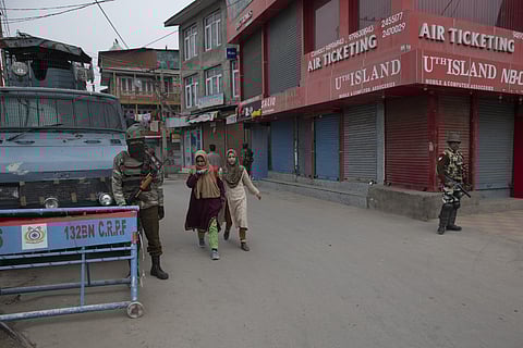 Kashmiri girls walks past Indian paramilitary soldiers standing guard during a strike on the death anniversary of separatist leader Maqbool Bhat in central Srinagar, Tuesday, Feb. 11, 2020. (Photo | AP)
