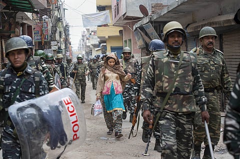 A woman walks along with security personnel following clashes over the new citizenship law in northeast Delhi. (Photo | PTI)