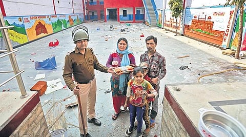 A policeman officer offers food to a security guard and his family at a school in Shiv Vihar where they were stuck during the riots. (Photo | Shekhar Yadav, EPS)