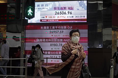 A woman walks past an electronic board showing Hong Kong share index outside a local bank in Hong Kong, Thursday, Feb. 27, 2020. Shares fell in Asia on Thursday after President Donald Trump announced the U.S. was stepping up its efforts to combat the viru