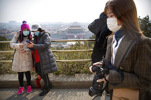 Visitors wearing face masks take photos at a park overlooking the Forbidden City in Beijing. (Photo | AP)