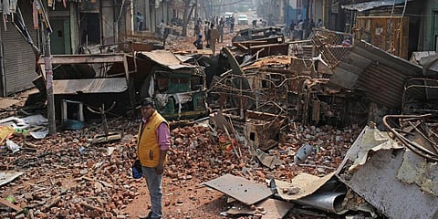 A Delhi municipal worker stands next to heaps of the remains of vehicles, steel cupboards and other materials on a street vandalized in violence. (Photo | AP)