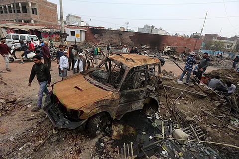 People walk next to the wreckage of motorcycles that were set on fire by a mob in a riot affected area after clashes erupted between people demonstrating for and against a new citizenship law at Mustafabad area in New Delhi on Friday.  (Photo | Shekhar Ya