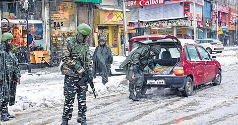A security personnel checks a vehicle as others stand guard during snowfall in Srinagar on Monday.  (Photo | PTI)