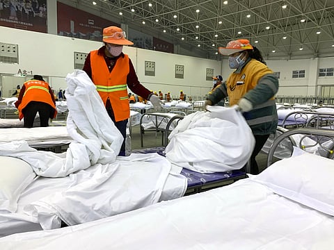 Workers arrange beds in a convention center that has been converted into a temporary hospital in China's Wuhan. (Photo | AP)