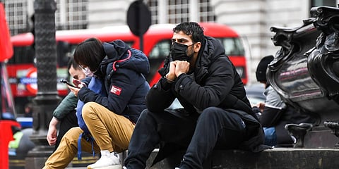 People wear face masks as they sit on the Shaftesbury Memorial Fountain in Piccadilly Circus, in London, Friday, March 13, 2020. (Photo | AP)