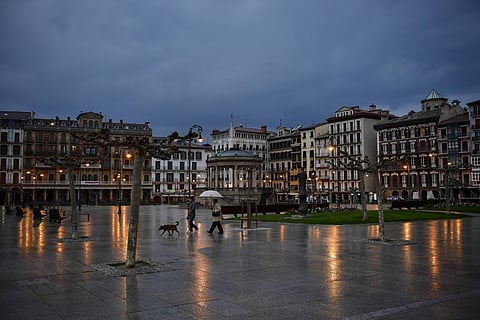 Pedestrians shelter from the rain under an umbrella while walking with a pet in an empty Plaza del Castillo square in the old city, in Pamplona, northern Spain. (Photo | AP)