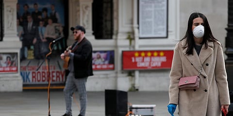 A street musician performs without ordinance as a woman with a face protection mask passes by at Piccadilly Circus after coronavirus outbreak in London. (Photo| AP)