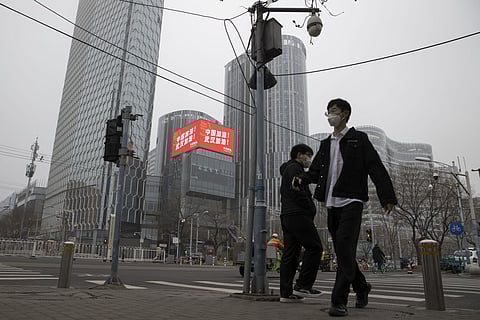 Residents walk past a retail and office district with a screen showing propaganda which reads 'Go China! Go Wuhan' as businesses slowly restart in Beijing on Sunday, March 8, 2020. (Photo | AP)