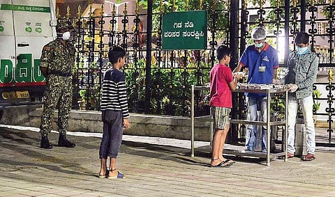 Volunteers distribute free food packets to the children of poor people at an Indira Canteen, in Bengaluru on Friday | Express