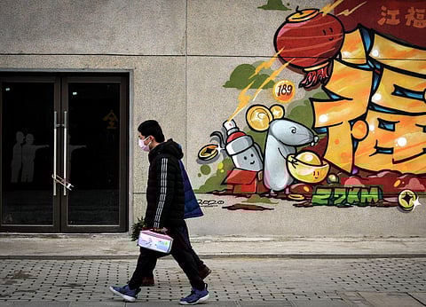 In this Saturday, Feb. 22, 2020, photo, a man wearing a protective face mask walks by a prosperity decoration on a closed building in Wuhan in central China's Hubei province. (Photo | AP)