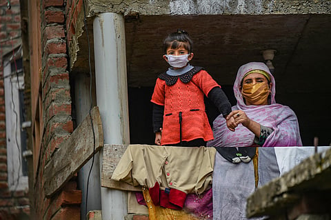 A woman and a child wearing masks look out from their house during a door-to-door surveillance by the health workers in a red zone area for COVID-19 amid the nationwide lockdown imposed to contain the spread of the novel coronavirus in Srinagar Thursday A