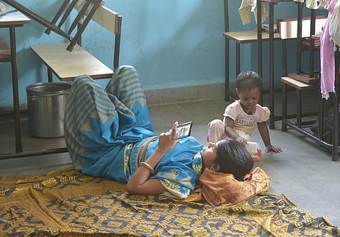 A woman watching videos on her phone at a shelter camp as her kid looks on. (Photo | PTI)