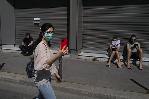 An entrepreneur from China wearing protective face mask walks in front Russian students taking the sun in Paris, Thursday, April 16, 2020 during a nationwide confinement to counter the COVID-19. (Photo | AP)