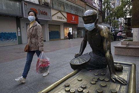 A resident walks through a partially closed retail street with a bronze statue covered with a face mask in Wuhan. (Photo | AP)