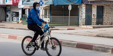 A man wearing a mask rides his bicycle after shopping in a deserted street of La Marsa, outside Tunis. (Photo| AP)