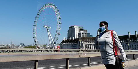 A woman wearing a protection mask to protect against coronavirus walks over Westminster Bridge in London. (Photo| AP)