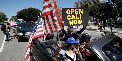 Protesters drive by in a convertible car during a rally calling for an end to California Governor Gavin Newsom's stay-at-home orders amid the COVID-19 pandemic. (Photo| AP)