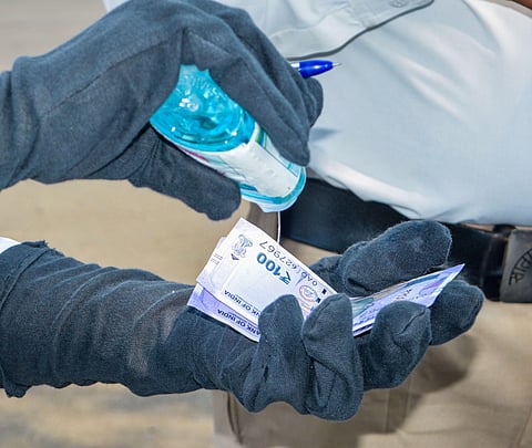 A police officer sanitizes currency notes after collecting them from commuters as a fine for flouting lockdown norms in the wake of coronavirus pandemic in Karad Saturday April 18 2020. (Photo | PTI)