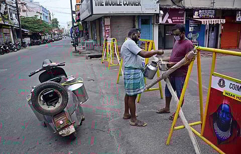 A resident of Big Bazaar street collecting milk from vendor from behind the barricade erected to prevent unwanted travel during the lockdown in effect in Coimbatore. (Photo | EPS/A Raja Chidambaram)