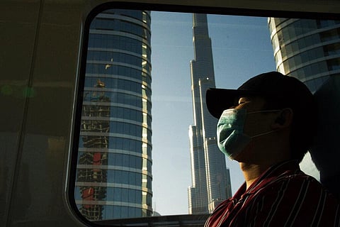 A commuter wearing a face mask to help curb the spread of the coronavirus, sleeps aboard the driverless Metro as it passes the Burj Khalifa, the world's tallest building, in Dubai, United Arab Emirates, Sunday, April 26, 2020. (Photo | AP)