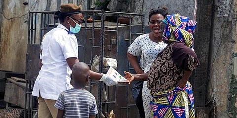 A health worker over COVID-19 awareness leaflets to people in Lagos, Nigeria. (Photo | AP)