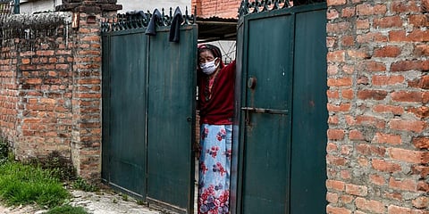 A woman stands at the gate of her home as she looks out on the empty street door in Kathmandu. (Photo| AFP)