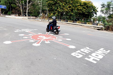 As Karnataka recorded its fifth death due to the coronavirus, a scooter passes over an COVID-19 awareness message painted on an empty road near Bengaluru's Anand Rao flyover. (Photo| Nagaraja Gadekal, EPS)