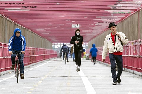 A jogger wearing a face masks runs in between a biker and a pedestrian not wearing masks as they make their way over the Williamsburg bridge in New York. (Photo | AP)