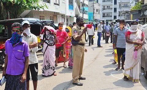 Residents await their turn at a ration shop as a police officer stands guard. (Photo | G Satyanarayana, EPS)