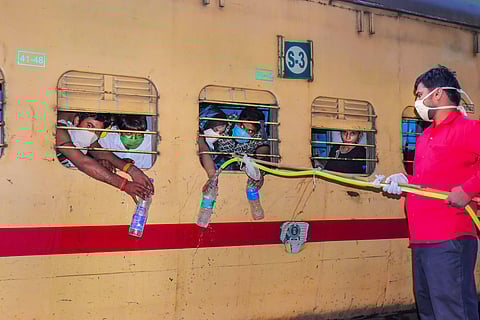 A railway employee maintains social distance as he provides drinking water to migrants leaving for their native places during the ongoing nationwide COVID-19 lockdown in Jabalpur Thursday May 21 2020. (Photo | PTI)