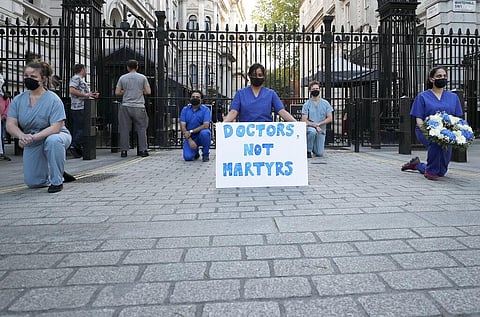 Doctors and nurses kneel in front of Downing Street ahead of the clap to remember colleagues who have died fighting the coronavirus pandemic in London, Thursday, May 28, 2020. (Photo | AP)