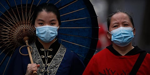A woman dressed in traditional costume holds an umbrella walks next to another woman both wearing a protective face masks to help curb the spread of the new coronavirus in Nanluonguxiang. (File photo| AP)