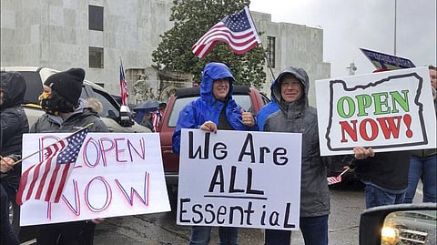 People hold signs protesting Oregon Gov. Kate Brown's executive order that shut down much of the state's economy. (Photo | AP)