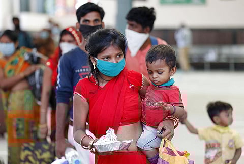 A migrant laborer carries a child and walk outside a railway station. (Photo | AP)