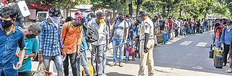 A policeman conducts checking of the migrant workers waiting in a queue to board buses for their native places in Surat | PTI